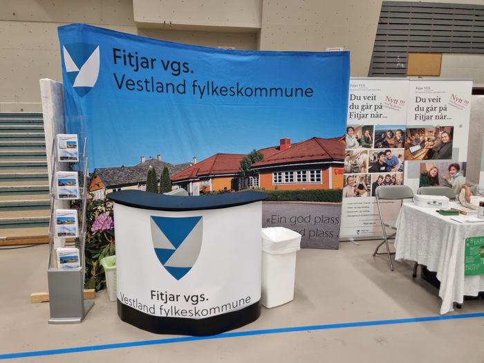 Eit bildete av ein stand på eit utdanningsmesse, med ein bardisk med logo og ein bakvegg med bilete av skulen