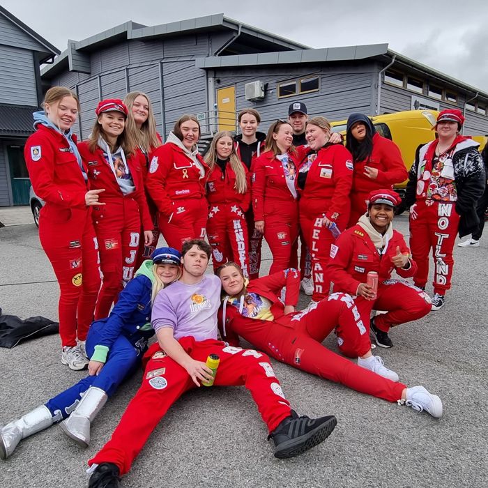 Eit bilete av ein gjeng elevar i russekjeledress som står samla framfor eit skulebygg. Nokre elevar sit på bakken.