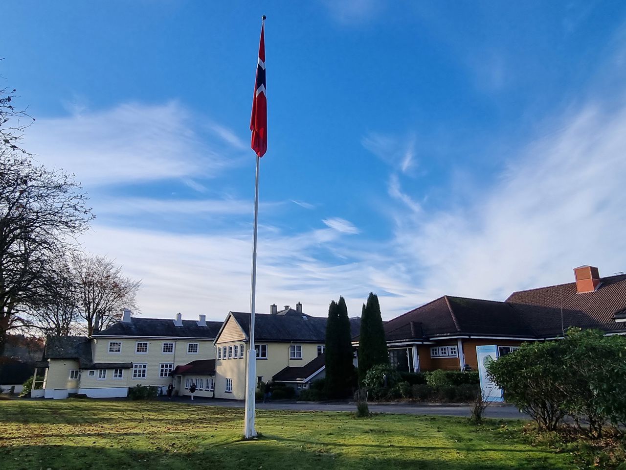 Eit norsk flagg på ei flaggstang, skulebygget i bakgrunnen