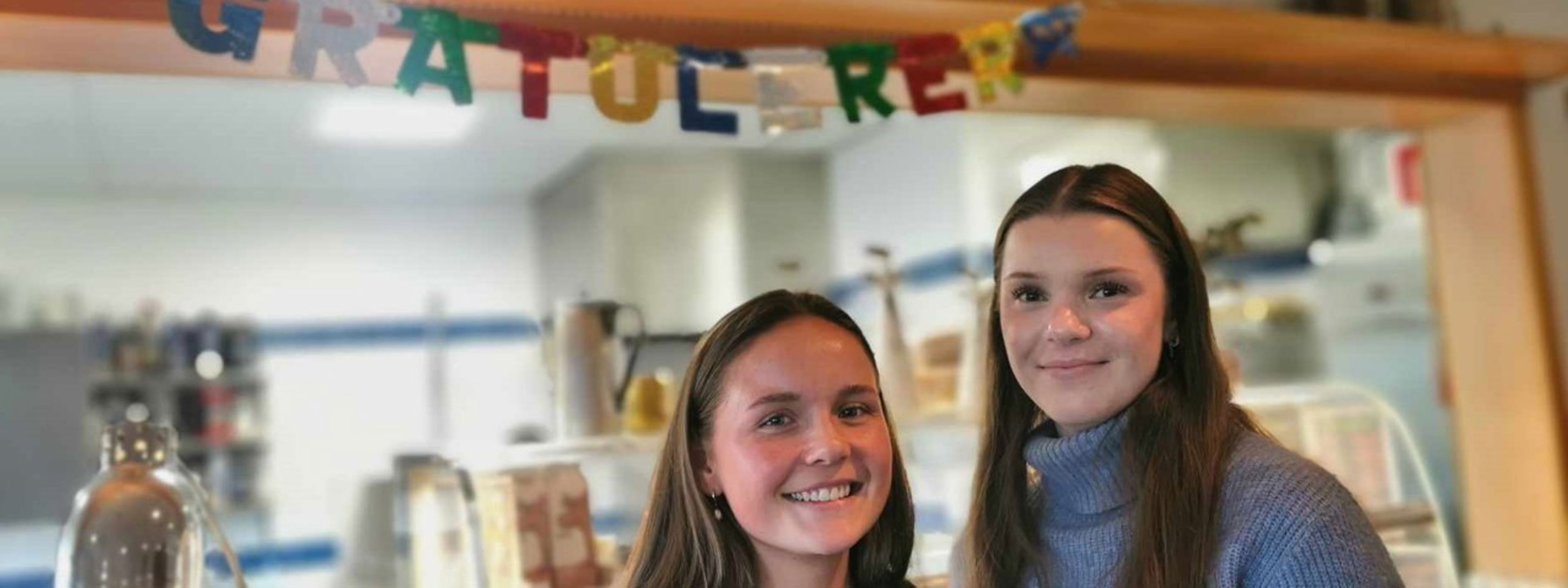 To elevar smiler i kantina framfor eit oppheng der det står "Gratulerer"